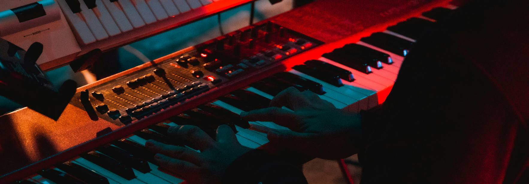 Una persona toca varios teclados en un ambiente iluminado con luces rojas y azules.