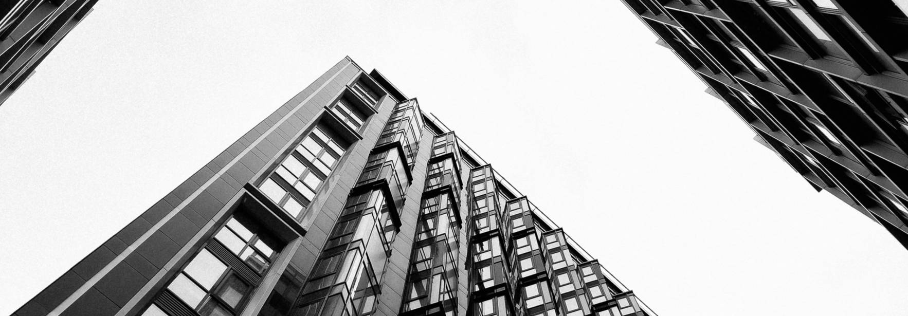 La imagen muestra un ángulo bajo de edificios modernos que se alzan hacia el cielo en blanco y negro.