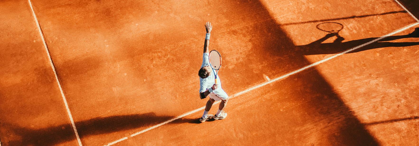 Un jugador de tenis sirve la pelota en una cancha de tierra batida.