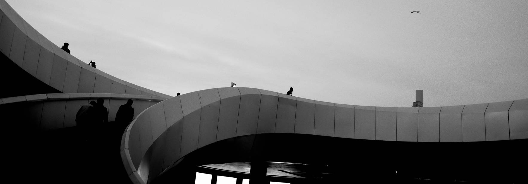 Una vista en blanco y negro de una estructura arquitectónica con personas en el borde y un cielo despejado.