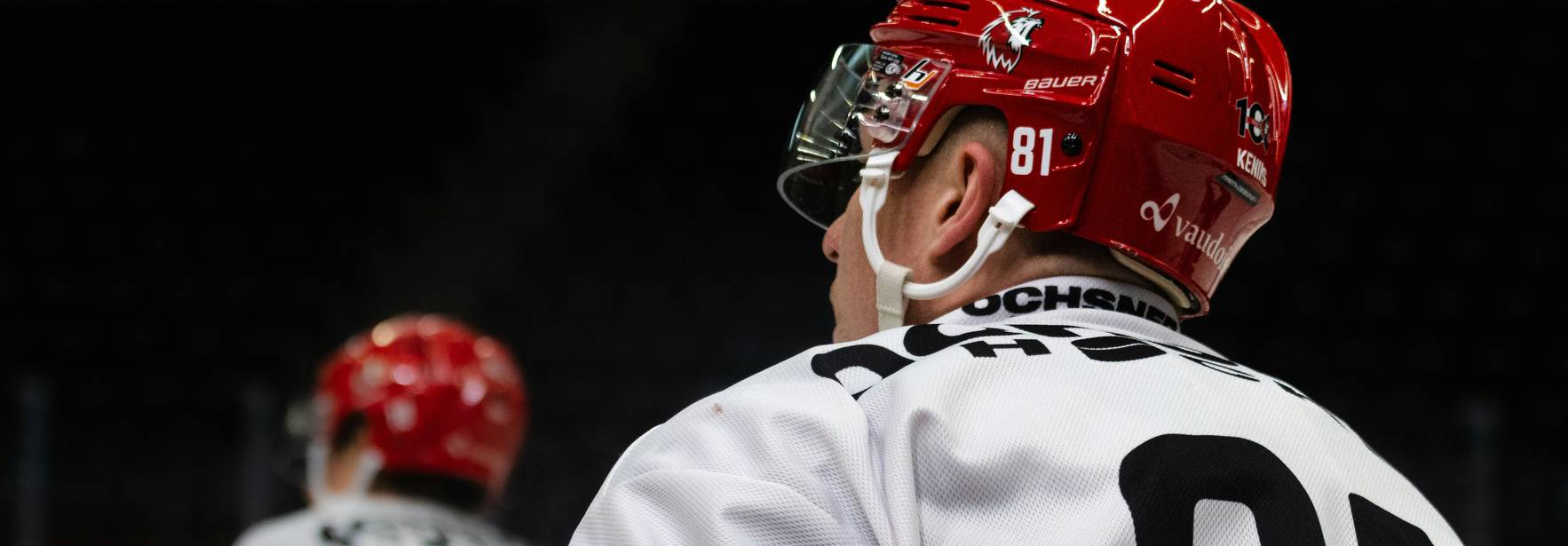 Un jugador de hockey sobre hielo con el número 81 en su camiseta observa el juego desde el banquillo.