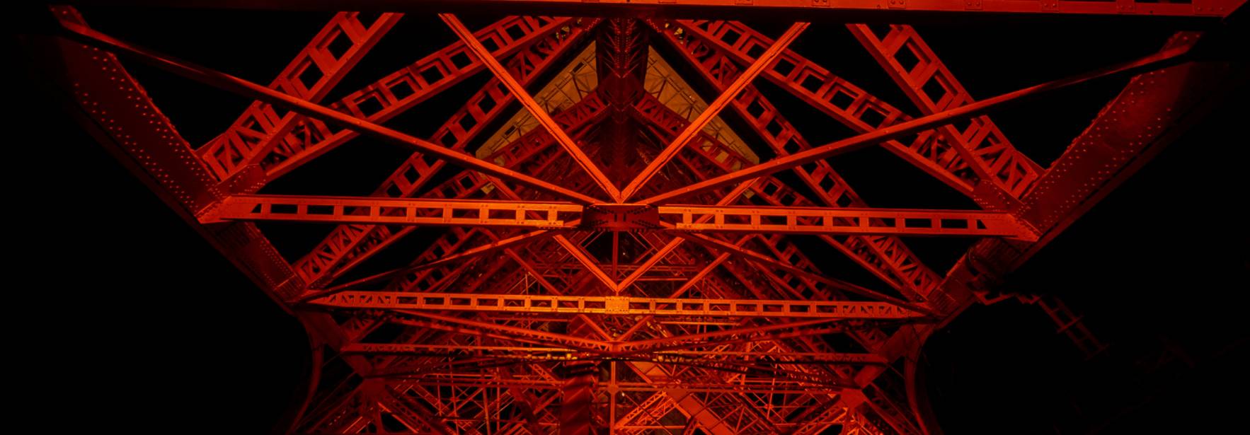 Estructura metálica iluminada de color rojo vista desde abajo.
