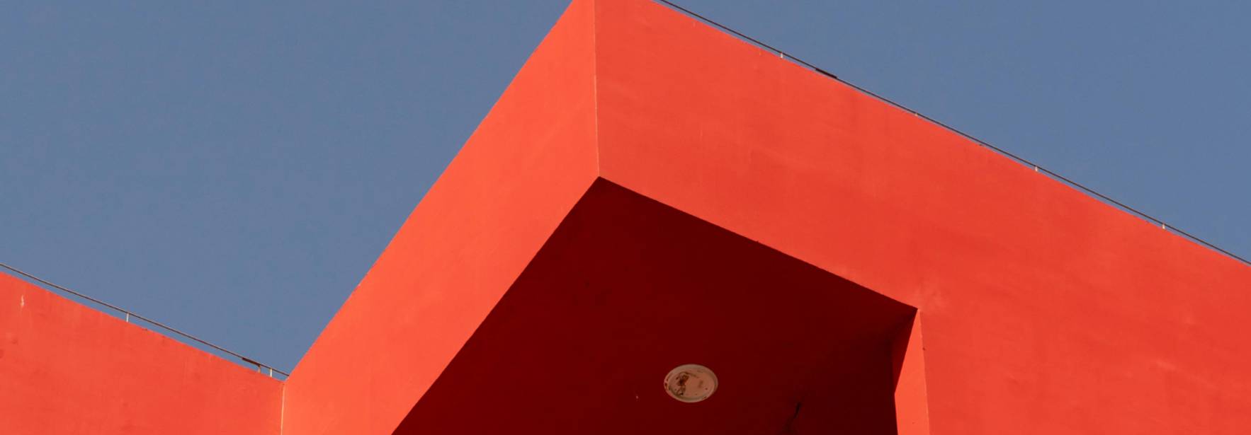 Esquina de un edificio moderno con un diseño angular y color rojo vibrante bajo un cielo azul.