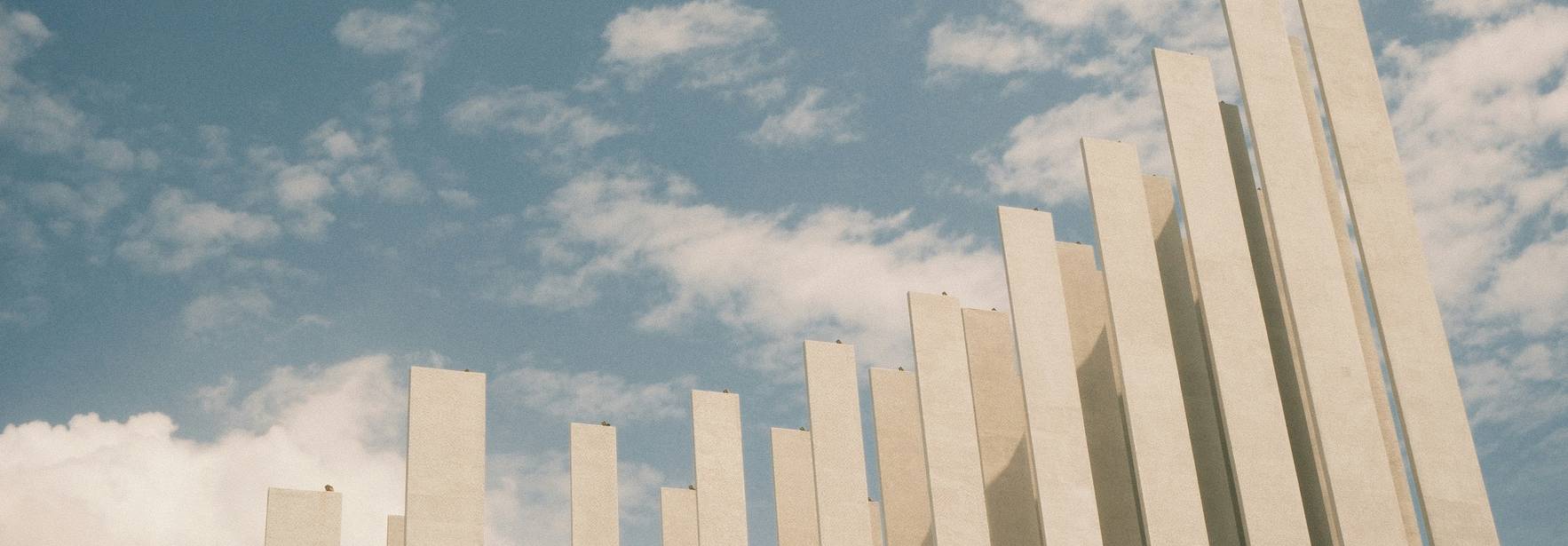 La imagen muestra una serie de columnas blancas que se elevan hacia el cielo bajo un fondo nublado.