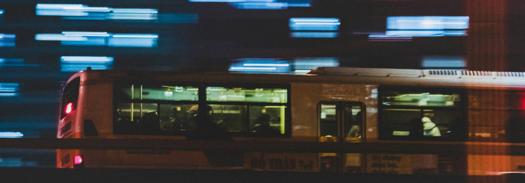 Un autobús se desplaza rápidamente por una ciudad iluminada, con luces borrosas de fondo que sugieren velocidad.