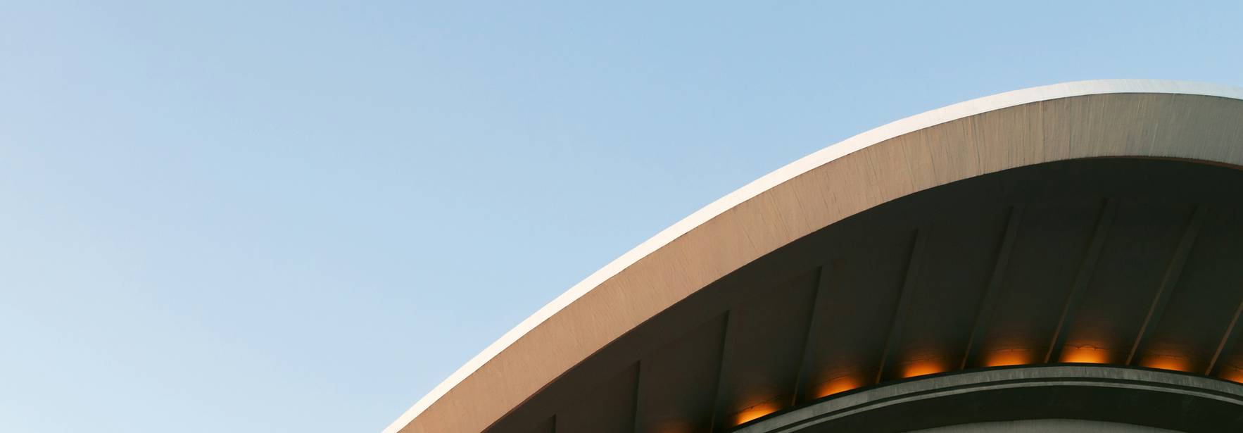 La imagen muestra la parte superior de un edificio con un diseño arquitectónico curvado y una iluminacion suave.