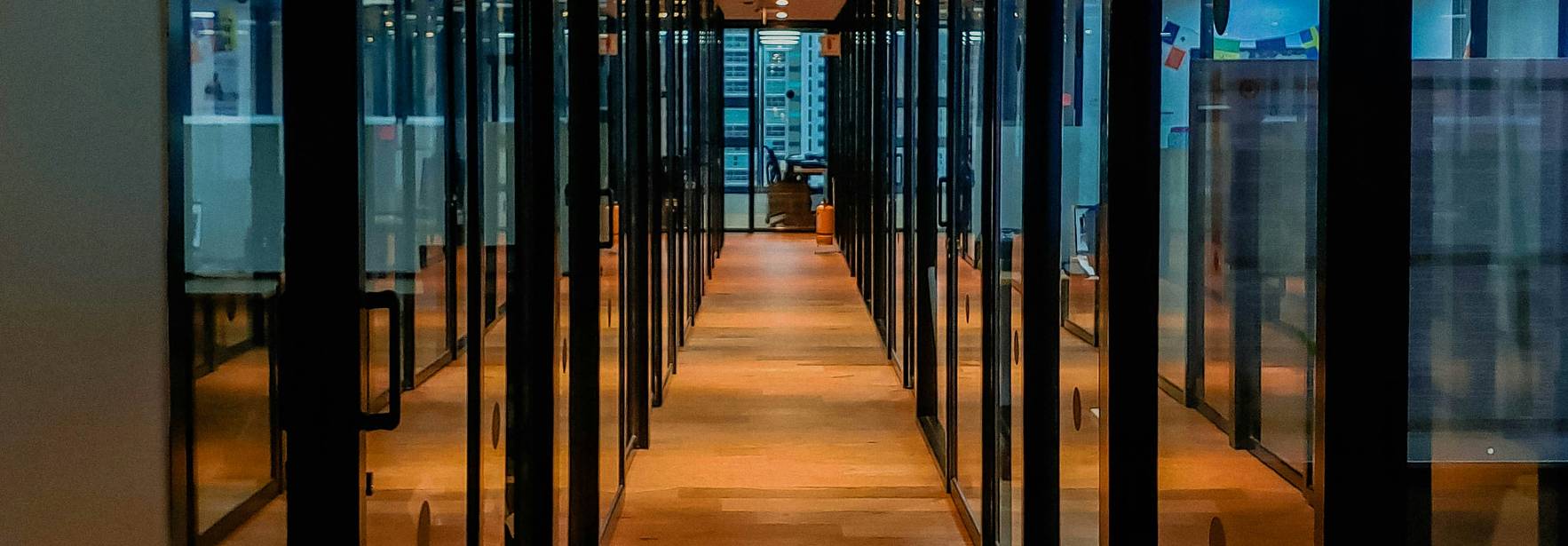 Pasillo moderno de oficinas con paredes de vidrio y suelo de madera.