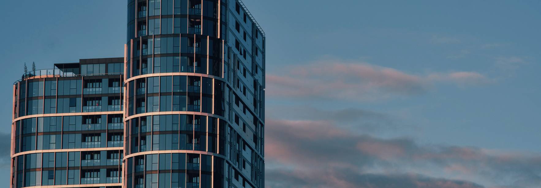 Edificios modernos de vidrio y acero bajo un cielo azul con nubes suaves.