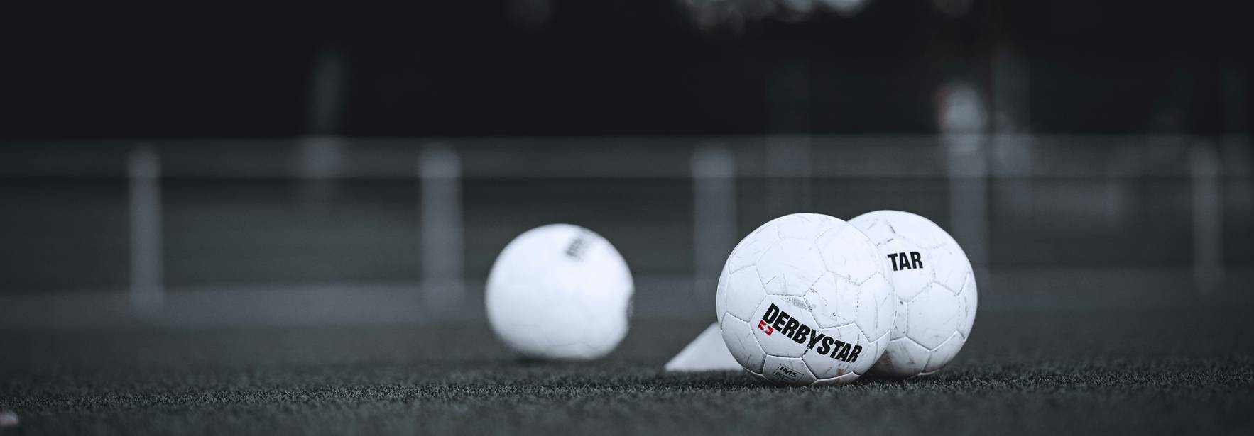 En la imagen se pueden ver varios balones de fútbol en un campo con césped sintético.