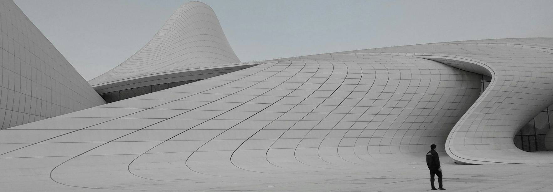 Un hombre se encuentra de pie frente a una arquitectura moderna con formas curvas y minimalistas.
