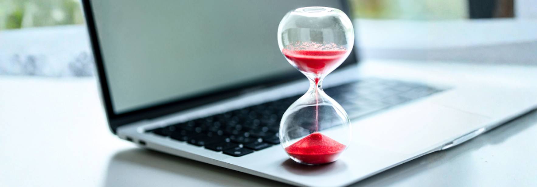 Un reloj de arena con arena roja colocado sobre un ordenador portátil.