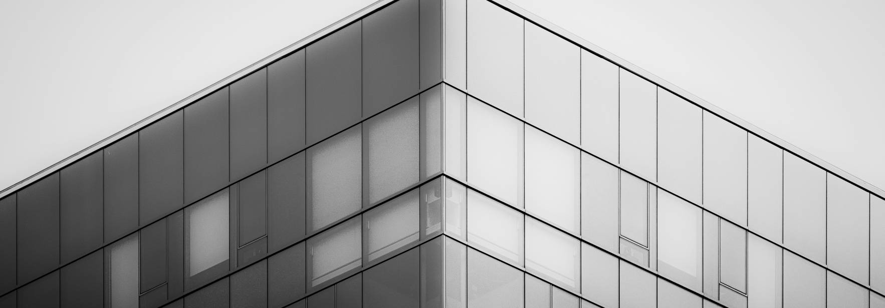 La imagen muestra la esquina superior de un edificio moderno de cristal en blanco y negro.