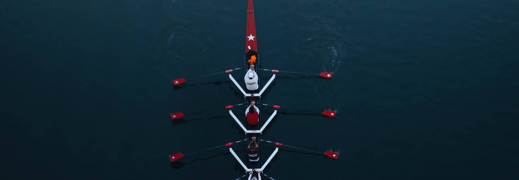 Vista aérea de un grupo de remeros en un bote sobre un agua tranquila.