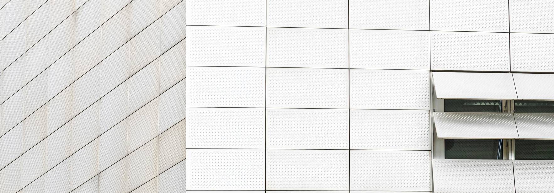 La imagen muestra una pared de edificio moderna con paneles claros y rejillas de ventilación.