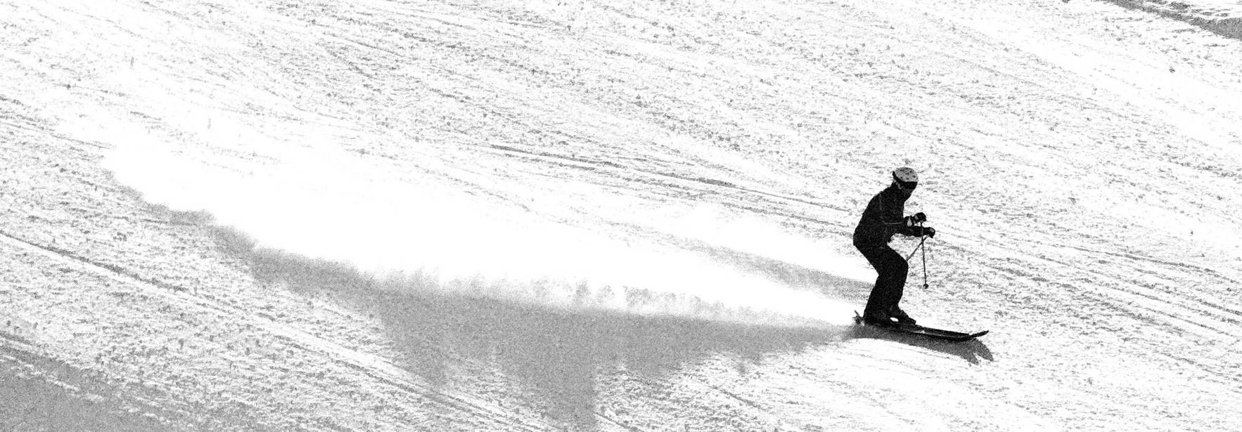 Un esquiador desciende por una pista nevada dejando una estela de nieve.