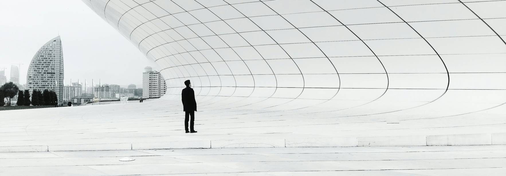 Un hombre de pie contempla una estructura arquitectónica moderna en un entorno minimalista.