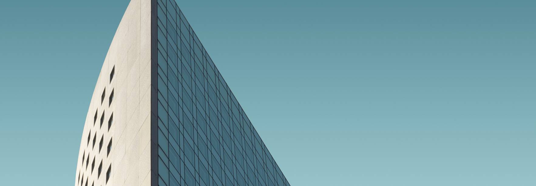 La imagen muestra la esquina superior de un edificio moderno con un diseño arquitectónico distintivo y un fondo azul claro.