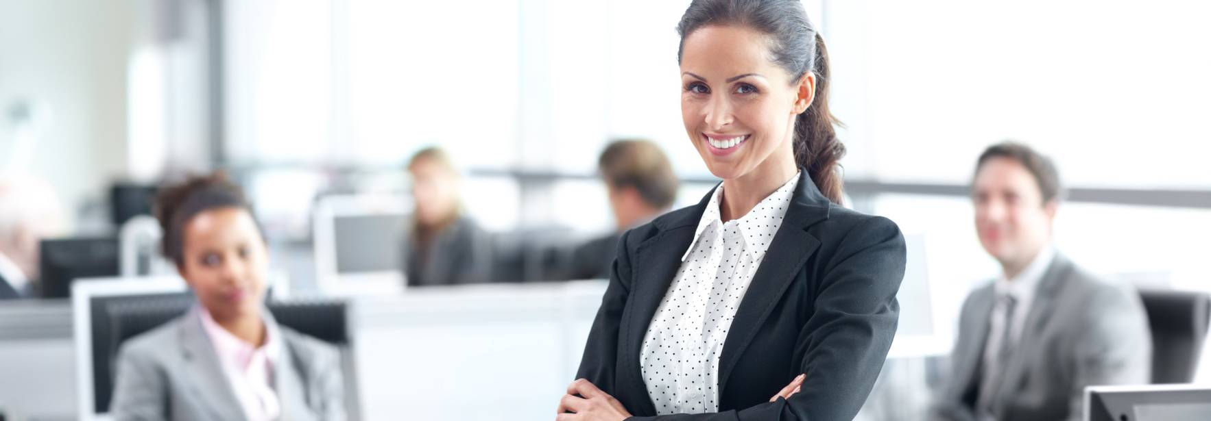 Una mujer sonriente en un entorno de oficina moderna, rodeada de colegas que trabajan.
