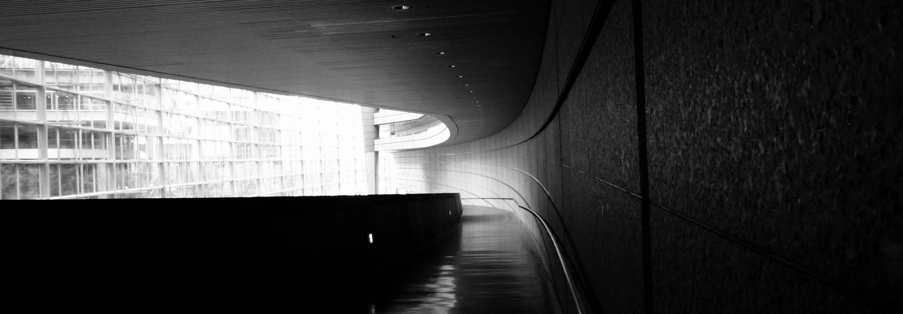 Una imagen en blanco y negro que muestra un pasillo curvado con iluminación suave y un fondo arquitectónico.