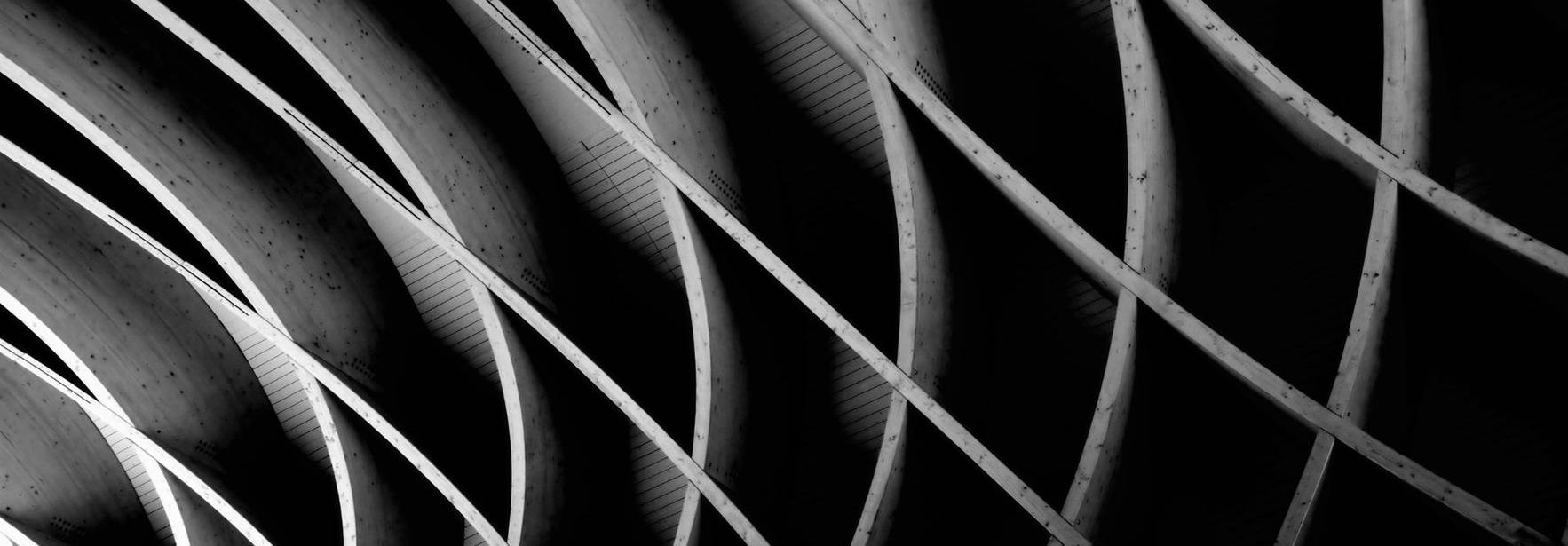 La imagen presenta una serie de líneas curvas y paralelas en tonalidades de blanco y negro, creando un efecto abstracto y arquitectónico.