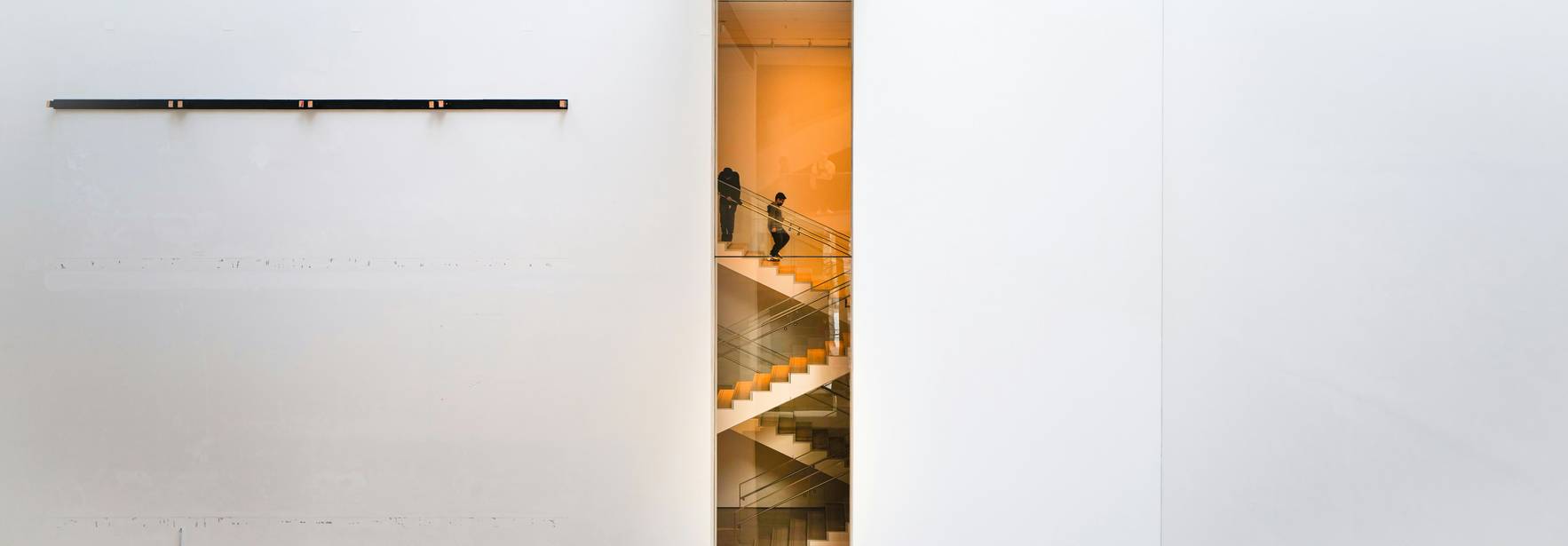La imagen muestra una escalera moderna vista a través de una abertura en una pared blanca.