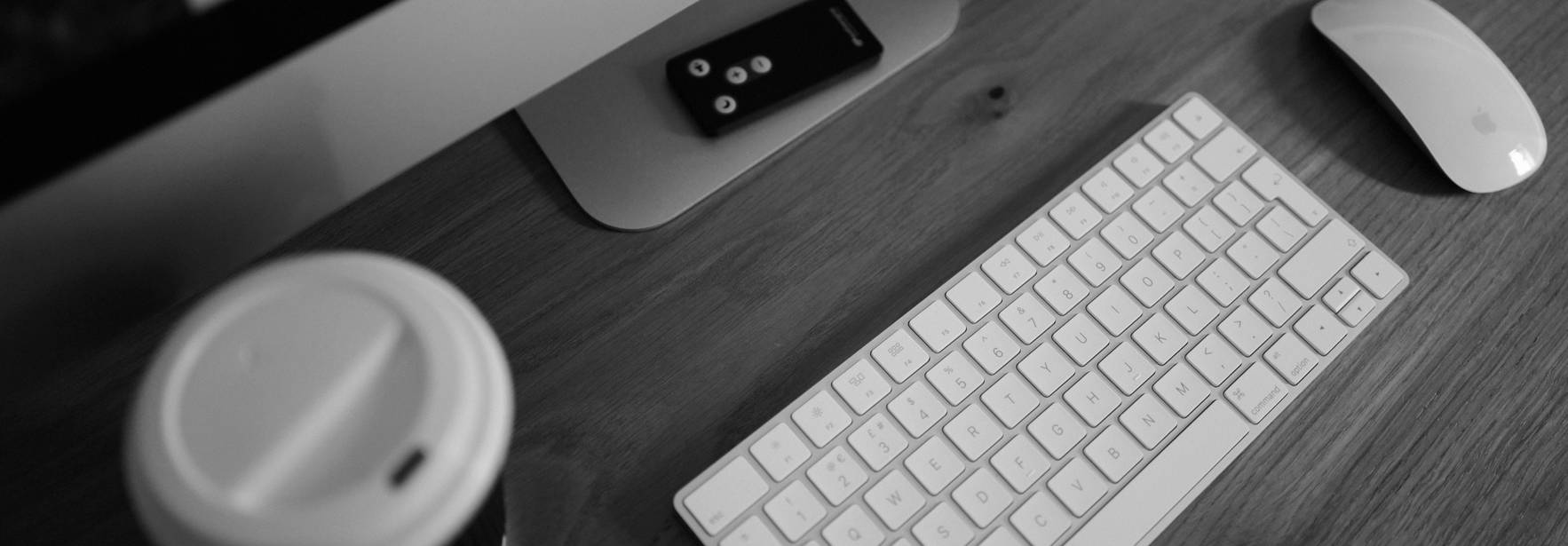 Una mesa de trabajo con un teclado, un mouse, un teléfono y una taza de café.