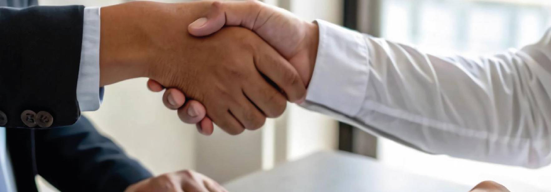 Dos personas se dan la mano en un acuerdo mientras una de ellas sostiene un documento en la mesa.