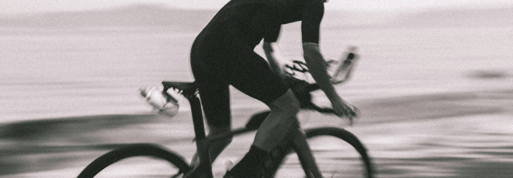 Un ciclista pedalea rápidamente frente a un paisaje costero difuminado.