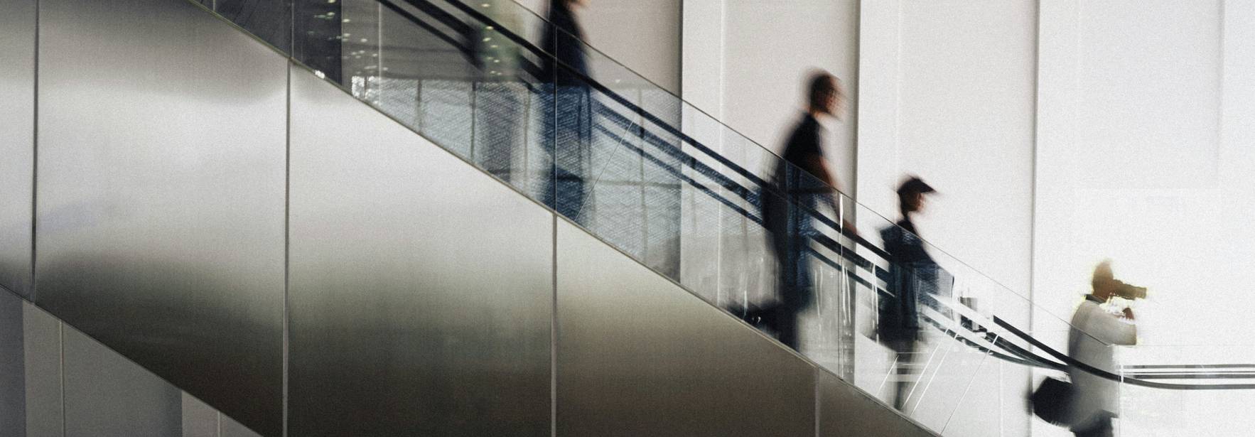 Una imagen que muestra a varias personas bajando por una escalera mecánica en un entorno moderno y minimalista.