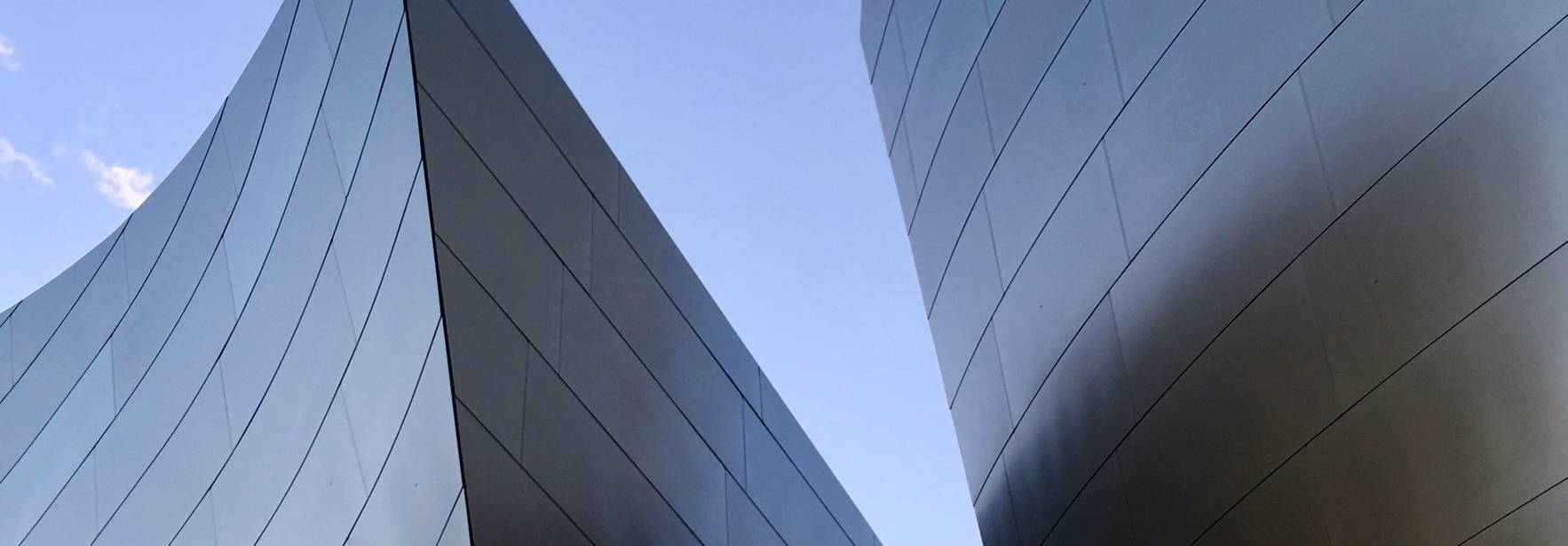 La imagen muestra dos estructuras arquitectónicas metálicas con formas curvadas contra un cielo azul.