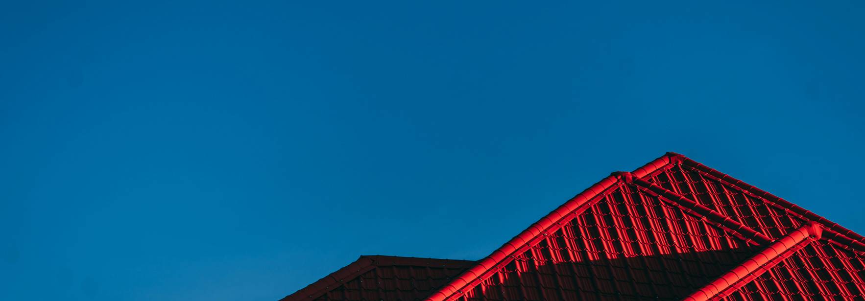 La imagen muestra el tejado de un edificio iluminado por una luz roja bajo un cielo azul despejado.