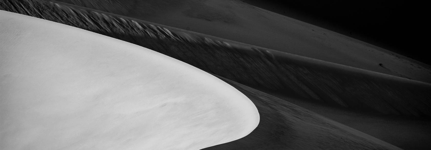 Una fotografía en blanco y negro que muestra las suaves ondulaciones de las dunas del desierto.