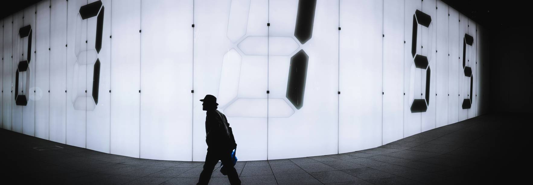 Un hombre camina frente a una pared iluminada con números grandes y brillantes.