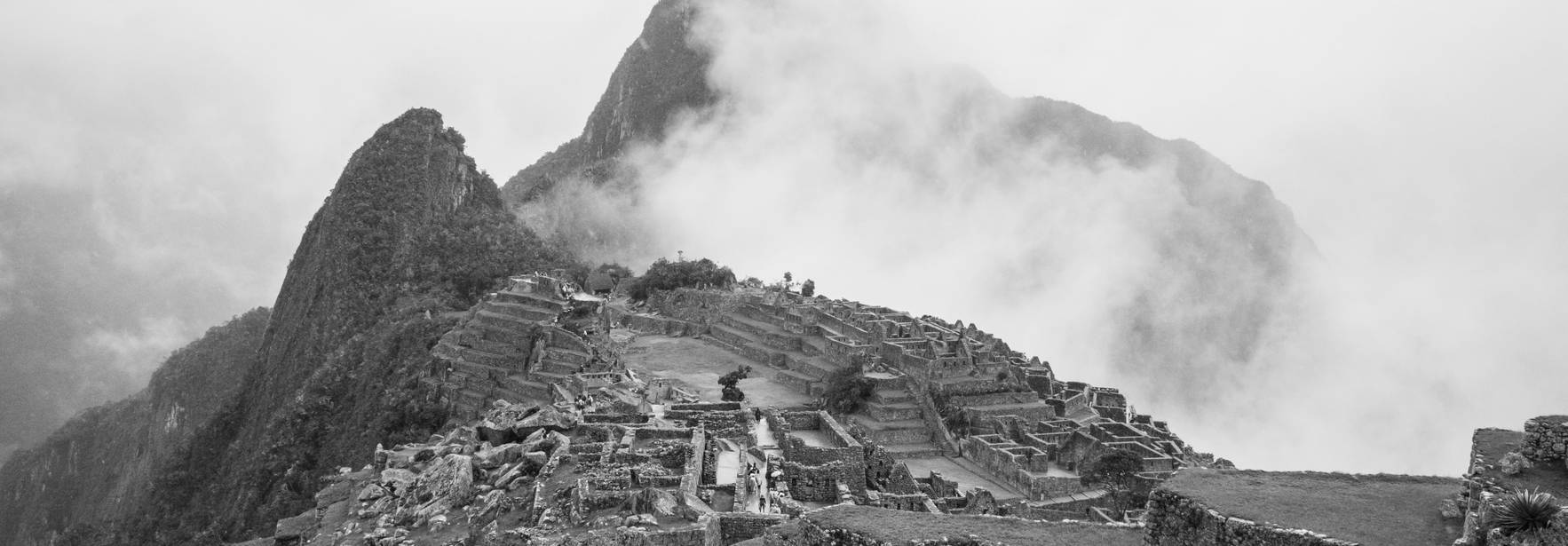 La imagen muestra las ruinas de Machu Picchu envueltas en nubes y neblina.