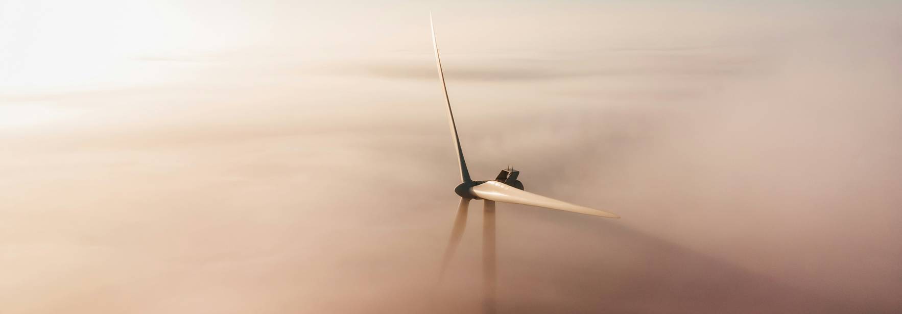 Una turbina eólica sobresale de un mar de niebla bajo un cielo despejado.