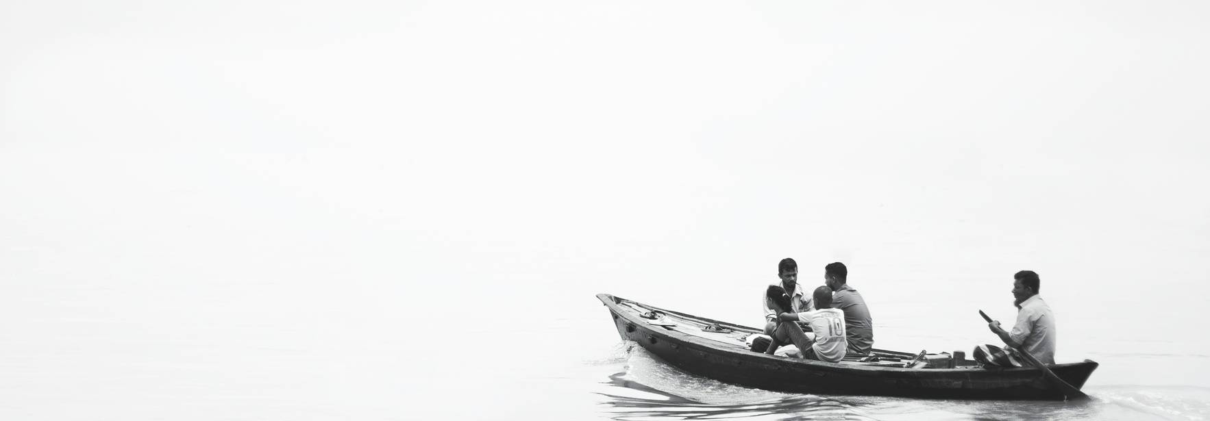 Un grupo de hombres navegando en una pequeña embarcación sobre un agua tranquila y neblinosa.