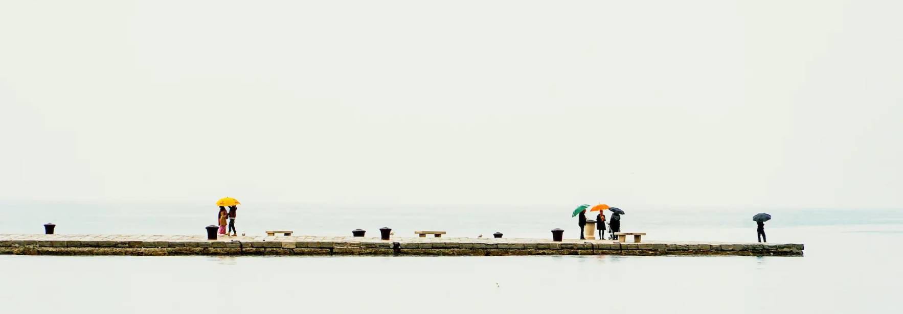Una escena en un muelle con personas trabajando bajo paraguas de colores en un día nublado.
