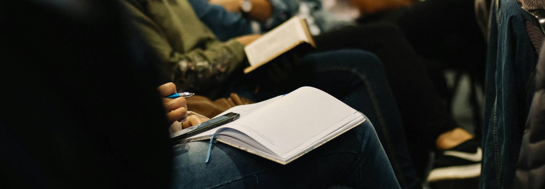 Un grupo de personas sentadas en un evento, algunas con cuadernos y tomando notas.