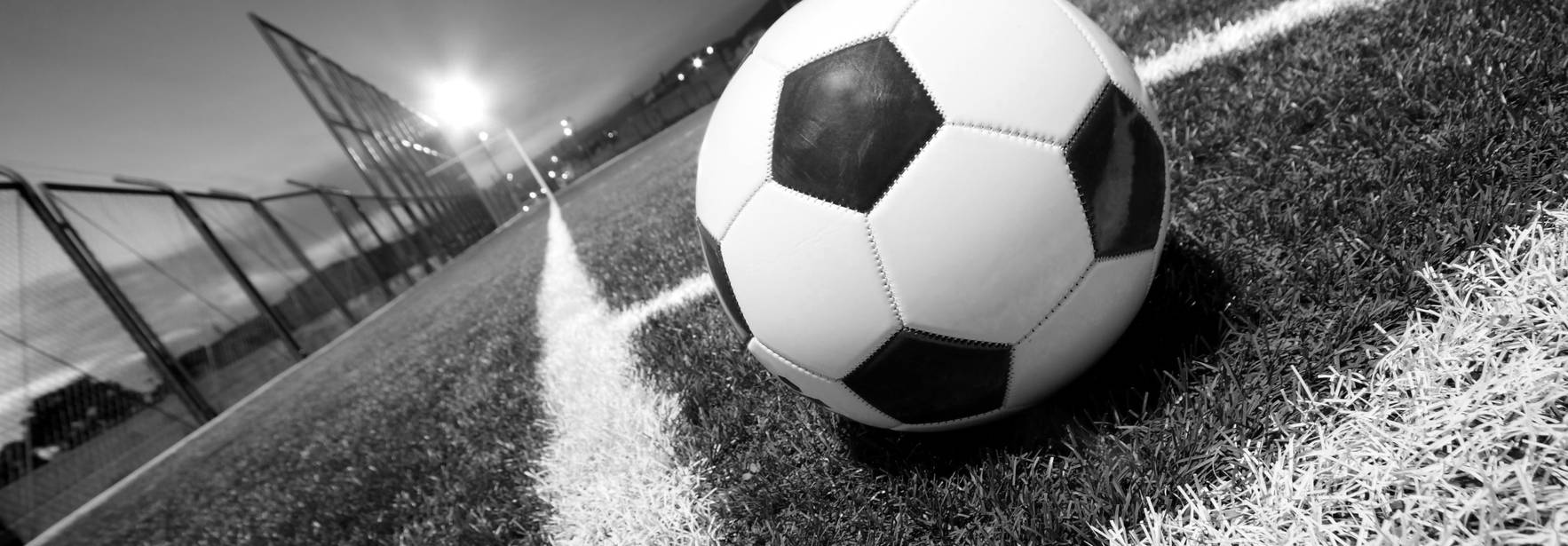 Un balón de fútbol descansa en la línea de banda de un campo de fútbol en blanco y negro.