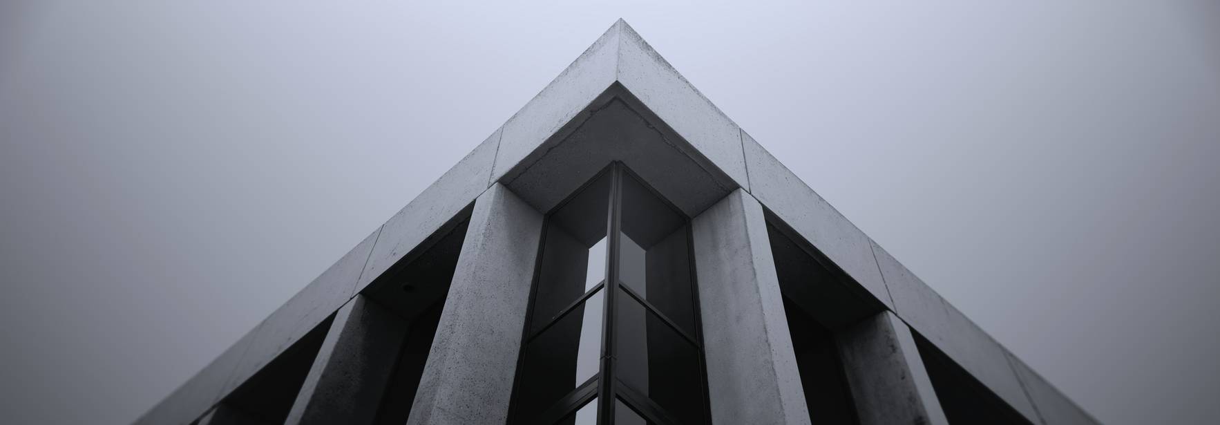 La imagen muestra la esquina superior de un edificio moderno con un diseño minimalista y un ambiente neblinoso.