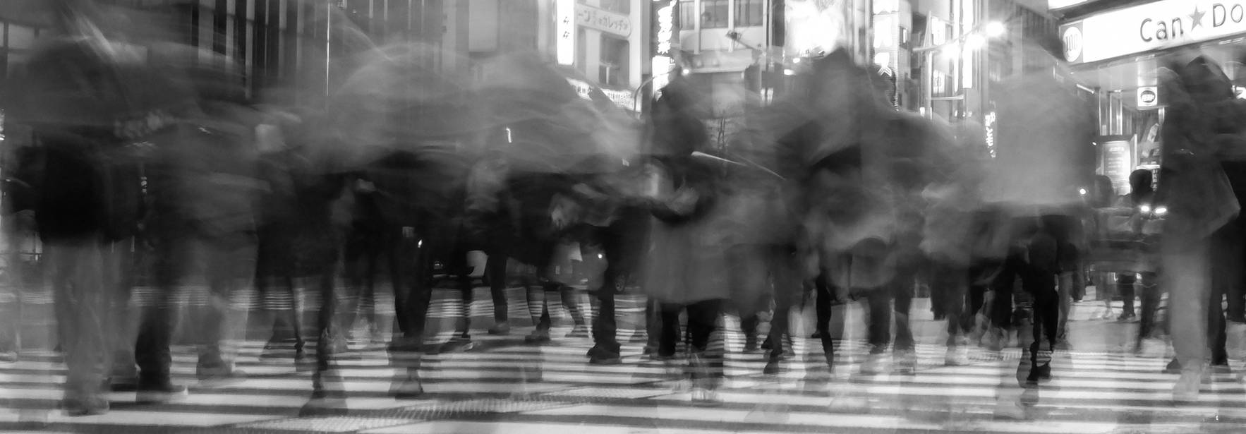 Una multitud de personas cruza una intersección peatonal en una ciudad moderna durante la noche.