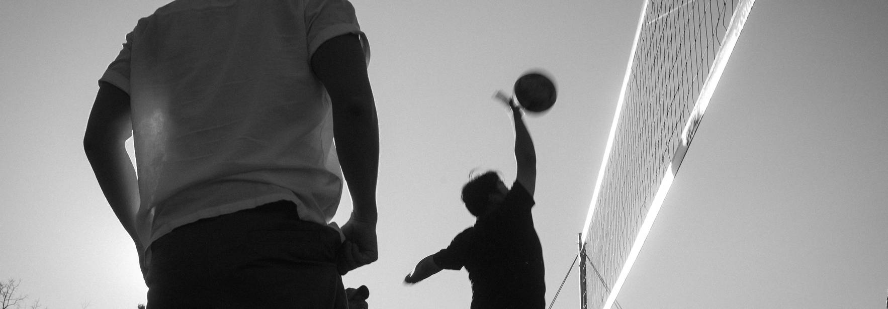 Una escena en blanco y negro de un grupo de personas jugando voleibol al aire libre durante el atardecer.