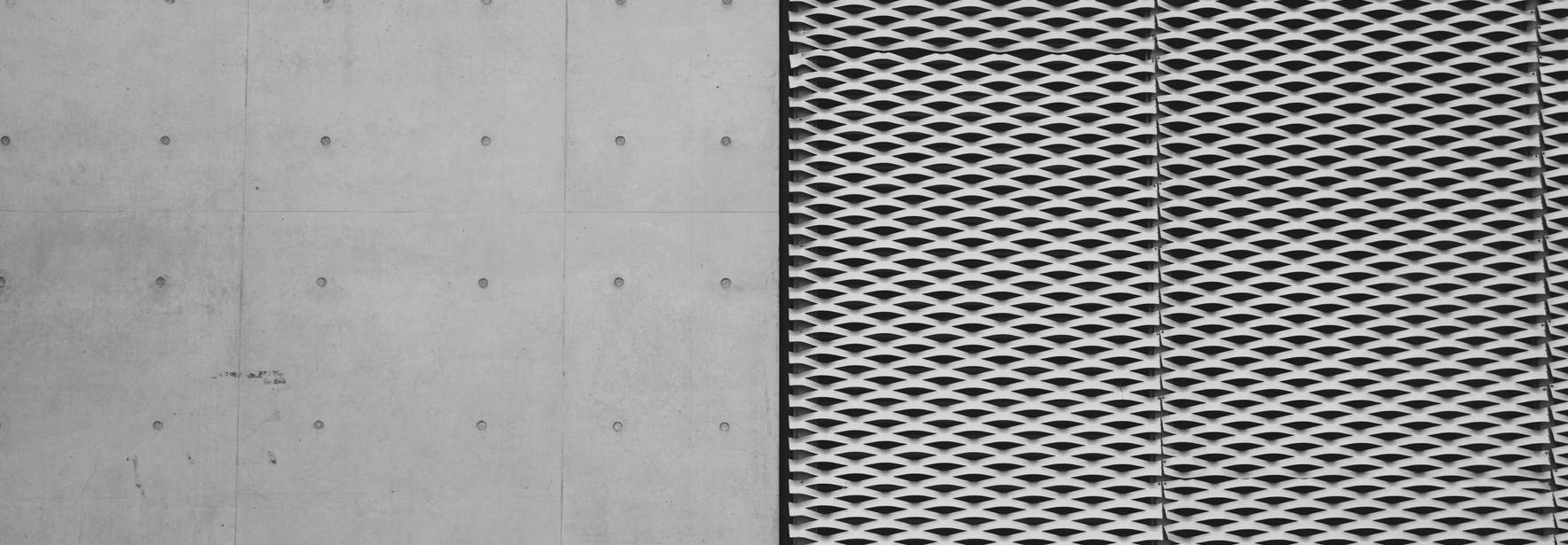 La imagen muestra una pared de concreto al lado de una superficie metálica con un diseño de rejilla en tonos claros.