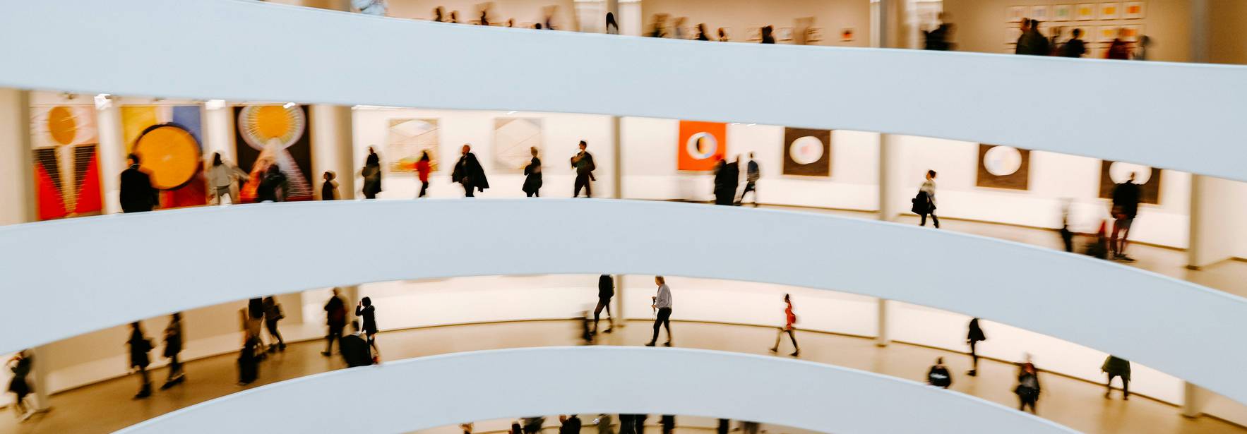 Una vista de un museo con varias personas caminando entre las exposiciones en un diseño arquitectónico curvo.