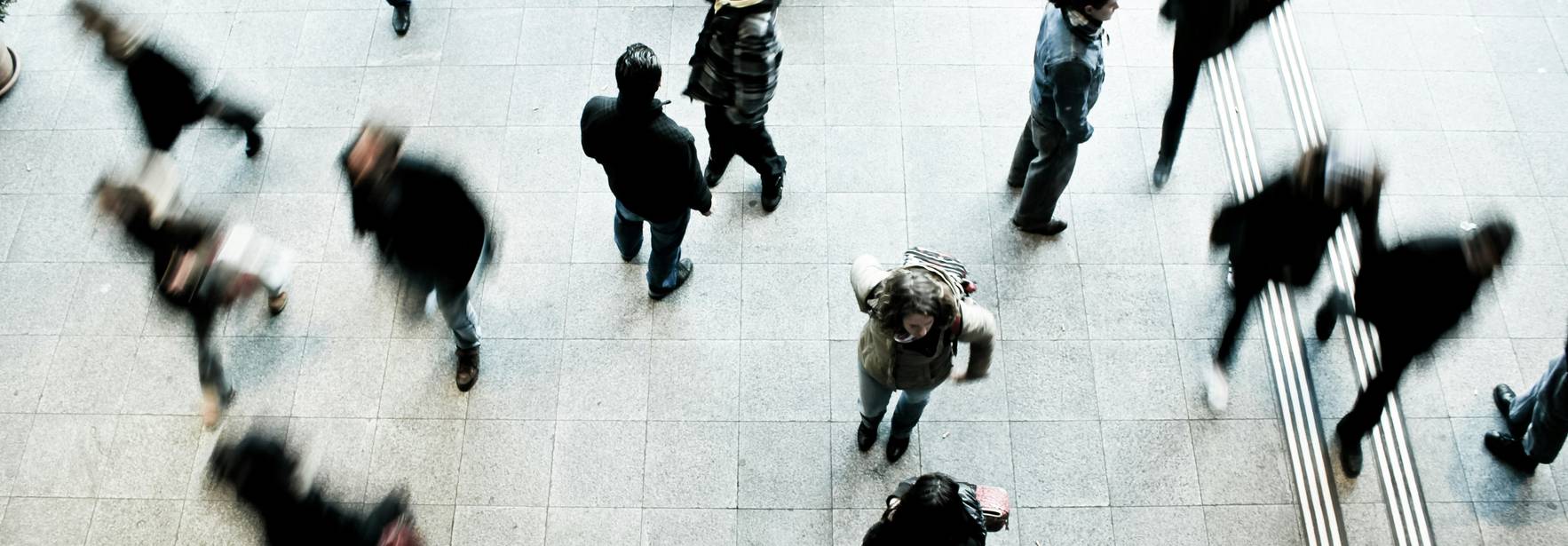 Una multitud de personas camina rápidamente sobre un suelo de loseta.