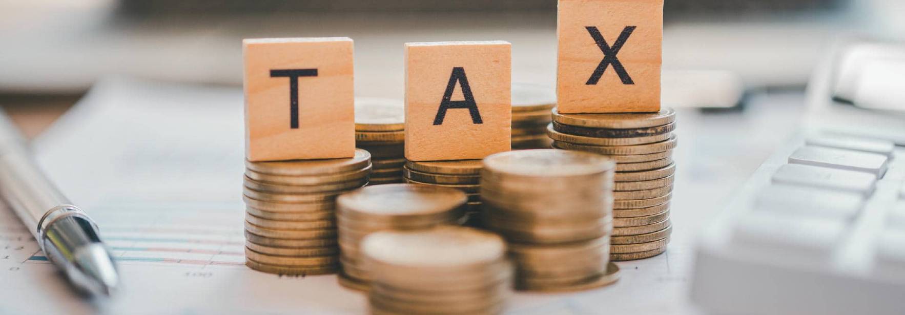 Una imagen que muestra monedas apiladas con bloques de letras que forman la palabra 'TAX'.