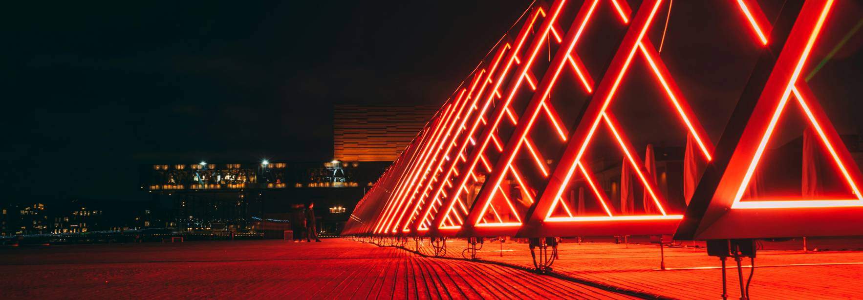 Una estructura triangular iluminada con luces rojas en un entorno nocturno.