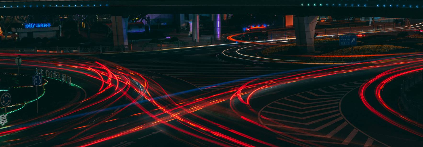 Una imagen nocturna de un cruce de carreteras con luces de coches creando un efecto de estela luminoso.