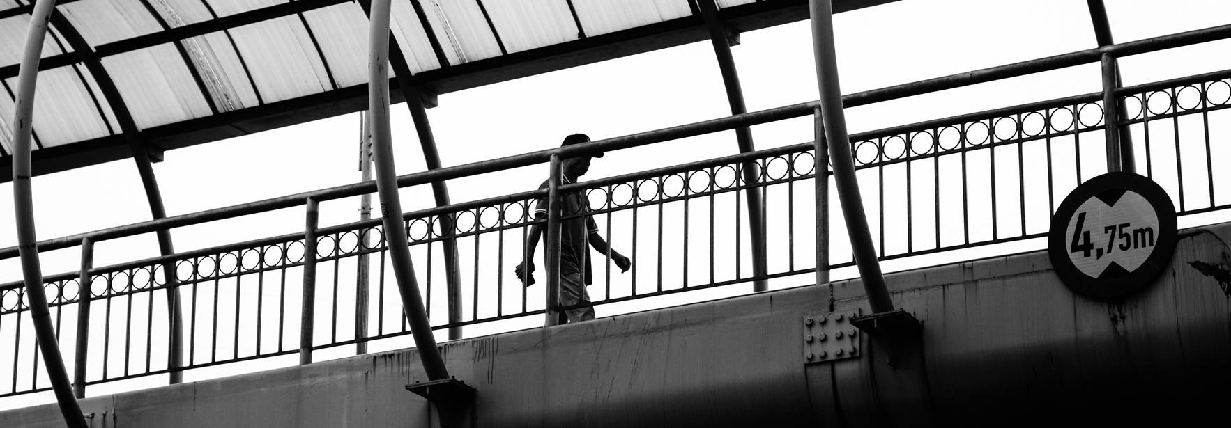 Una persona camina sobre un puente peatonal en blanco y negro.