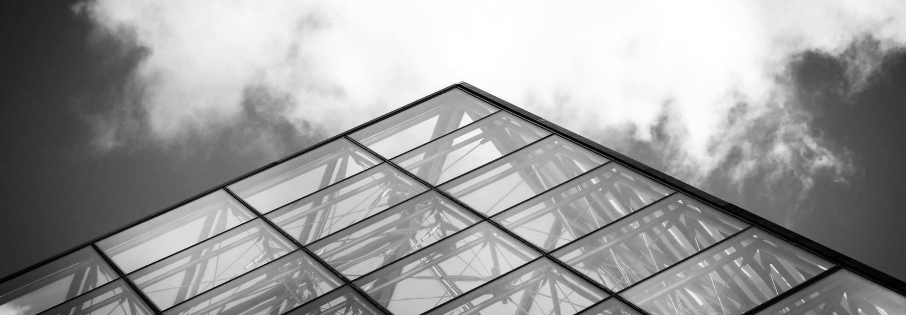 Una imagen en blanco y negro de una estructura moderna con una esquina de cristal que se eleva hacia el cielo.